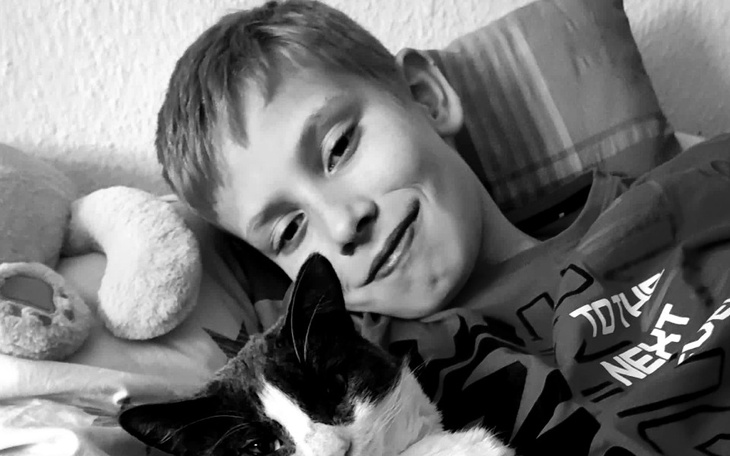 Chłopiec leżący z kotem, uśmiechnięty i zrelaksowany.