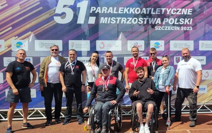 Grupa ludzi na zawodach paraolimpijskich, wszyscy uśmiechnięci.