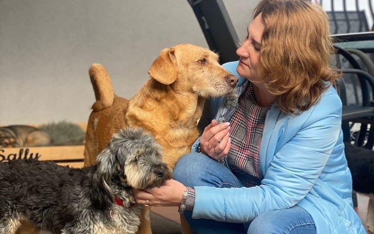 Kobieta przytulająca dwa psy, uśmiechnięta i szczęśliwa.