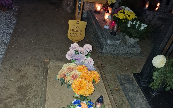 Grób z kwiatami i tabliczką z imieniem i datami.