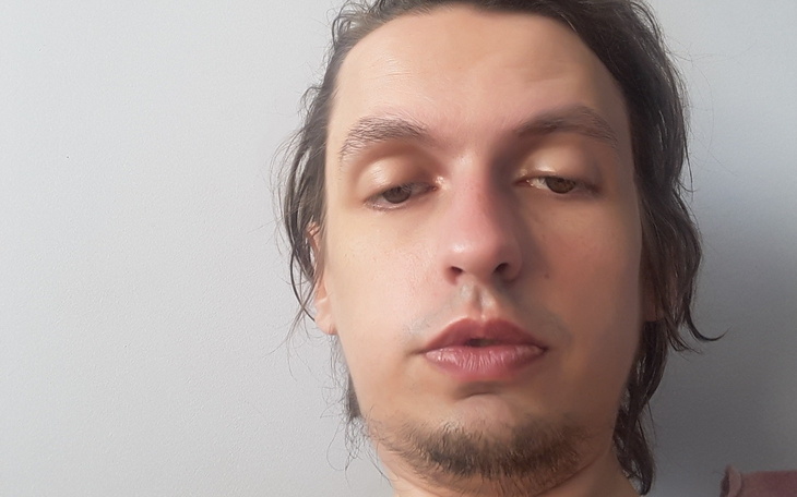 Mężczyzna z długimi włosami, patrzący w stronę kamery.