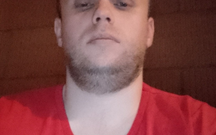 Mężczyzna w czerwonej koszulce, patrzący w kamerę.