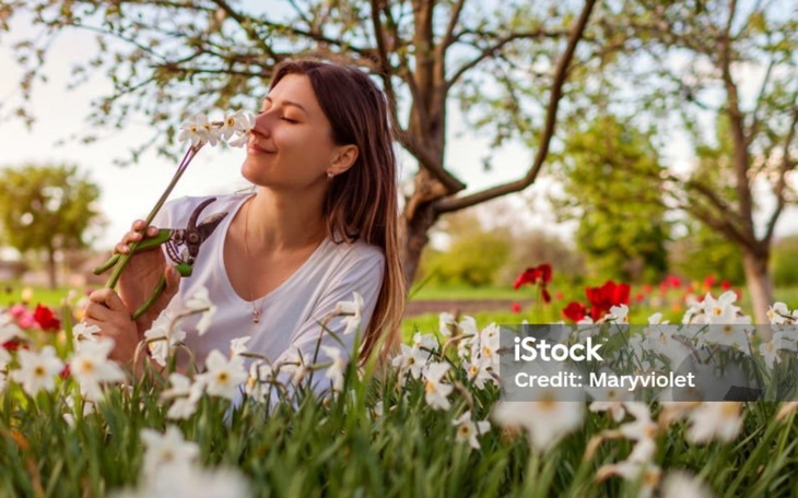 Kobieta w ogrodzie, wąchająca kwiaty.