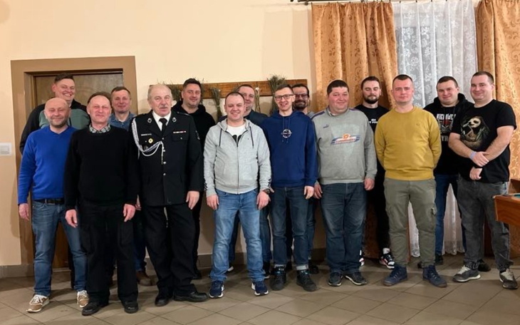 Grupa mężczyzn w mundurach strażackich i cywilnych na spotkaniu.