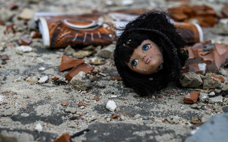 Zniszczona lalka leżąca na gruzie, z odłamkami wokół.