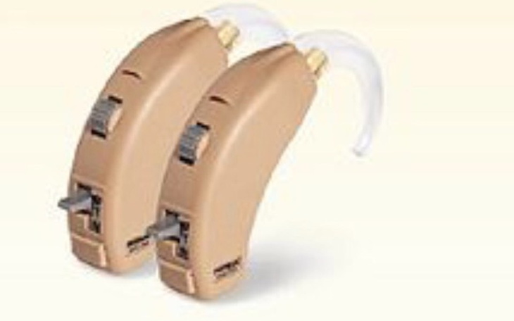 Dwa aparaty słuchowe w kolorze beżowym, z przezroczystymi wkładkami.