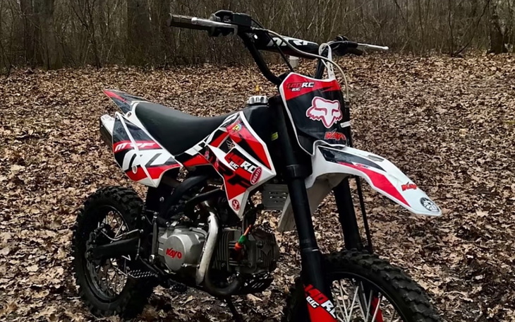 Motocykl terenowy w kolorach czerwonym i czarnym na tle leśnym.