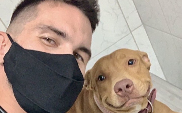 Mężczyzna w masce z psem, oboje uśmiechnięci.