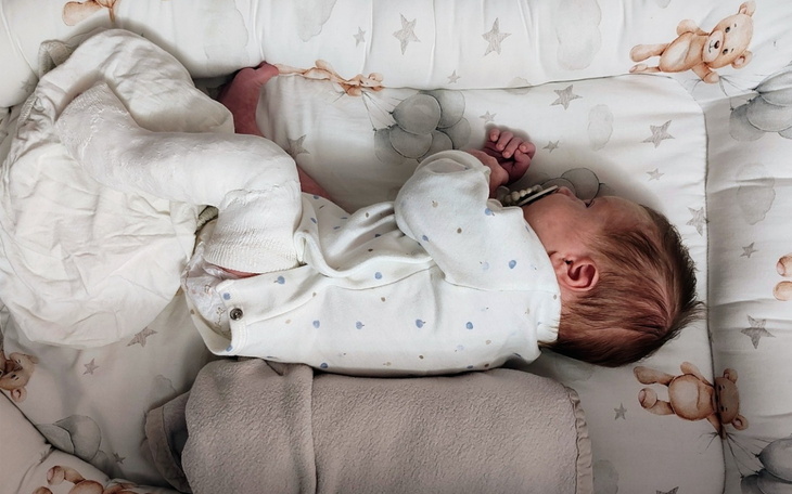 Noworodek śpiący w łóżeczku, w otoczeniu kocyków.