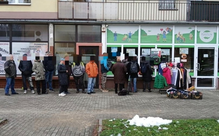 Ludzie stojący w kolejce przed sklepem z odzieżą używaną.