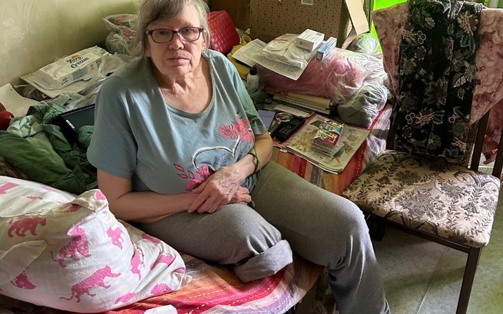 Kobieta siedząca na kanapie w zabałaganionym pomieszczeniu.