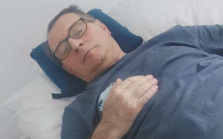 Mężczyzna leżący na łóżku, z ręką na sercu, w spokojnej pozycji.