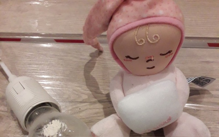 Pluszowa lalka siedząca obok żarówki, na drewnianej podłodze.