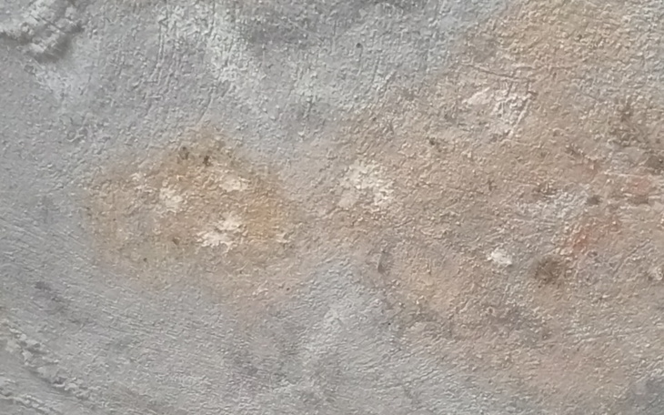 Zbliżenie na szaro-beżową powierzchnię, z widocznymi plamami.
