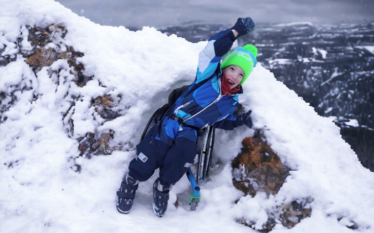 Chłopiec w wózku inwalidzkim, bawi się w śniegu.
