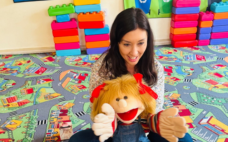 Kobieta z lalką na tle kolorowego dywanu w przedszkolu.