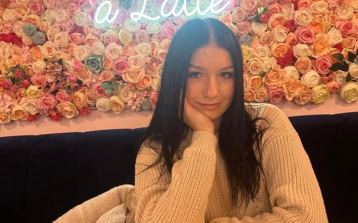 Młoda kobieta w swetrze, pozująca na tle kwiatów.