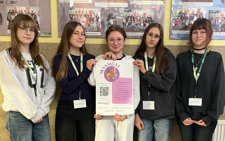 Grupa pięciu dziewcząt pozujących z plakatem w rękach.