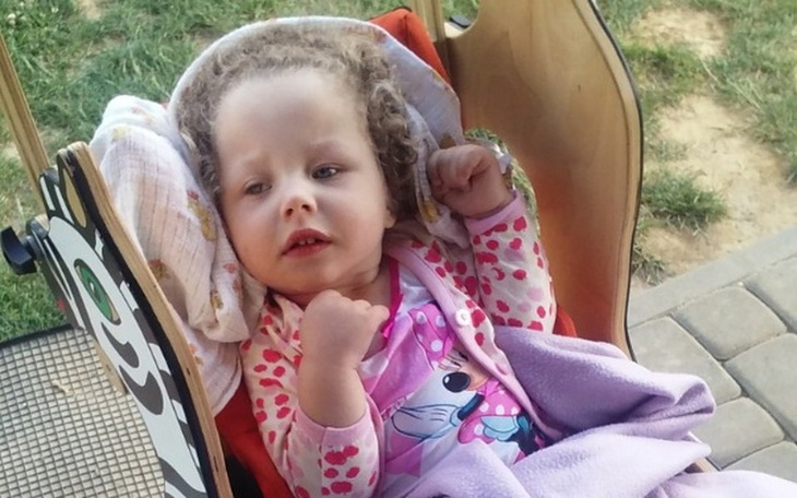 Dziewczynka w wózku, ubrana w różowy sweterek, z uśmiechem na twarzy.