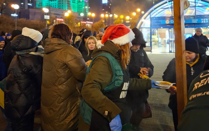 Osoby w ciepłych ubraniach, rozdające jedzenie w zimowej scenerii.