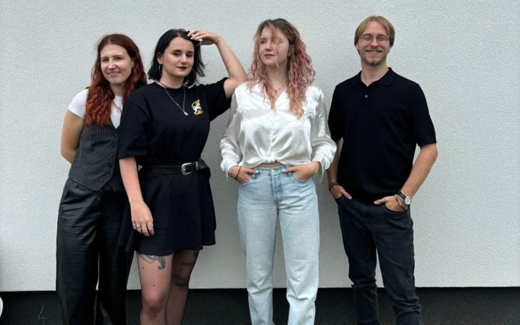 Cztery osoby pozujące na tle białej ściany, uśmiechnięte.