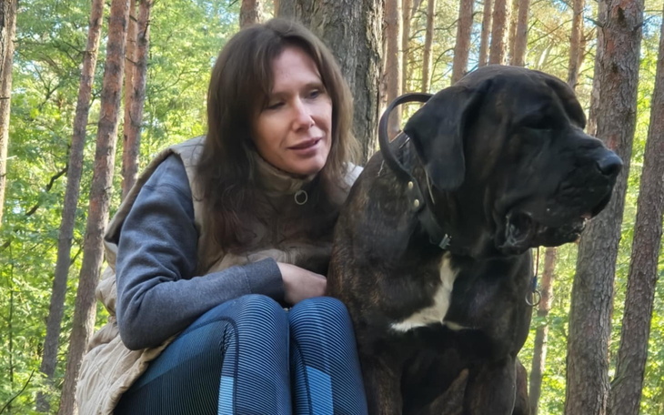 Kobieta siedząca z psem w lesie, w otoczeniu drzew.