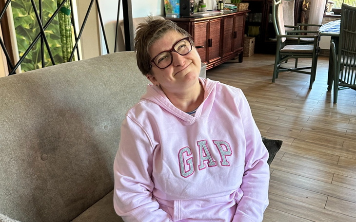 Uśmiechnięta kobieta w różowej bluzie siedząca w salonie.