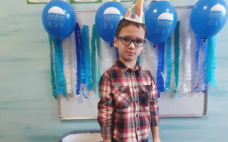 Chłopiec w okularach z kapeluszem urodzinowym, obok balony i dekoracje.