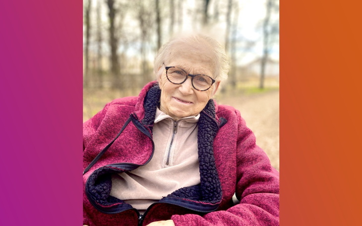 Starsza kobieta w okularach, uśmiechająca się na świeżym powietrzu.