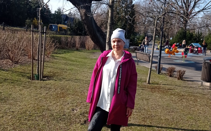 Kobieta w różowym płaszczu na tle parku.