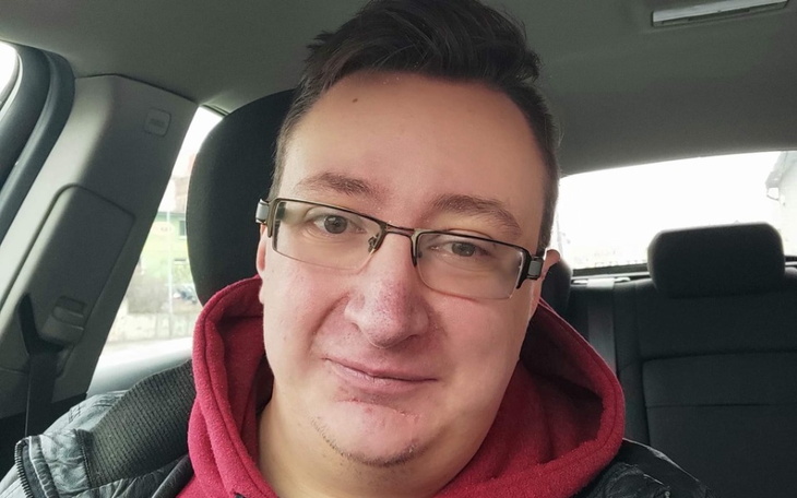 Mężczyzna w samochodzie, uśmiechający się do kamery.