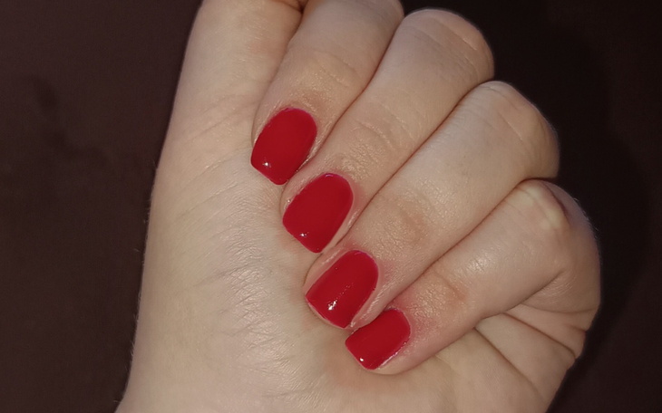 Czerwony manicure na dłoni, z błyszczącym wykończeniem.