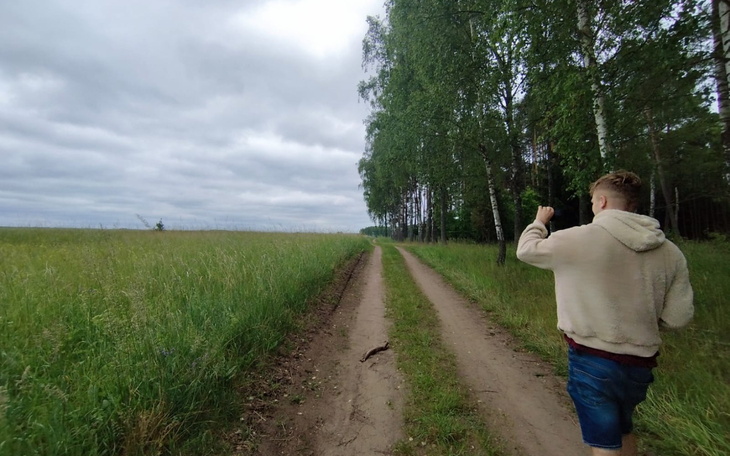 Mężczyzna spacerujący po leśnej drodze, otoczony drzewami.