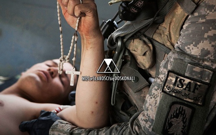 Żołnierz trzyma różaniec, pomagając rannemu mężczyźnie.