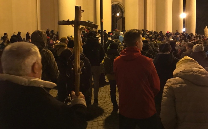 Tłum ludzi z krzyżem na tle budynku.