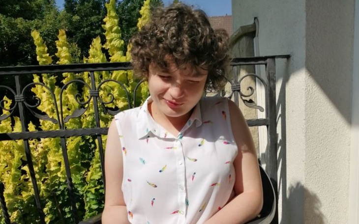 Młoda dziewczyna siedząca na balkonie, otoczona roślinami.