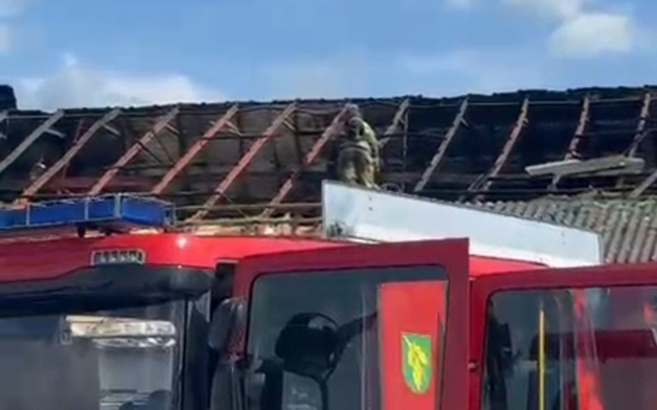 Strażak na dachu budynku, obok wóz strażacki.