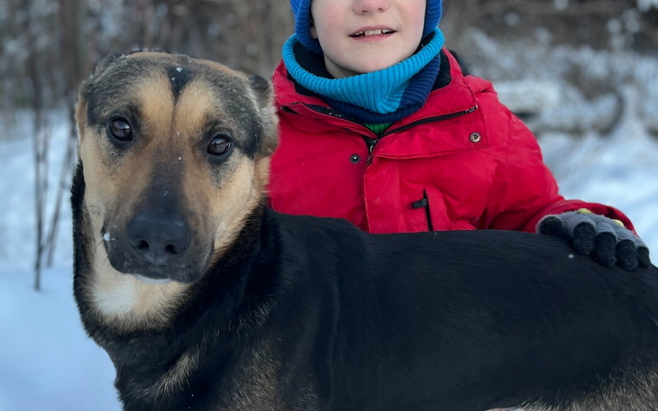 Chłopiec w czerwonej kurtce z psem na tle zimowego krajobrazu.