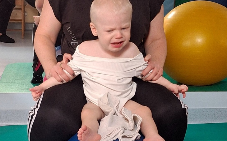 Małe dziecko siedzące na piłce, wyrażające niezadowolenie.