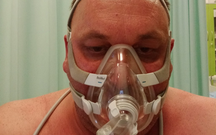 Mężczyzna w masce tlenowej, patrzący w obiektyw.