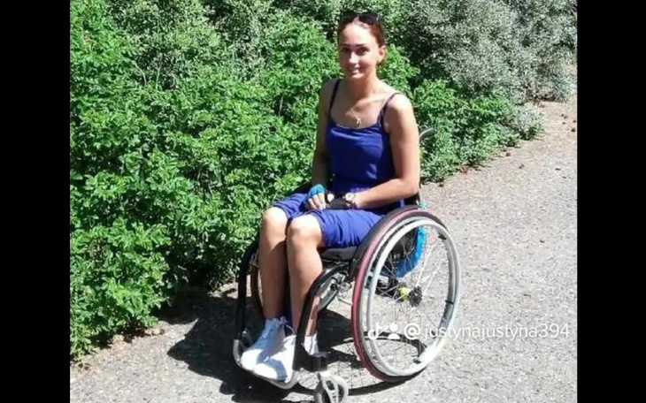 Młoda kobieta w wózku inwalidzkim na tle zieleni.