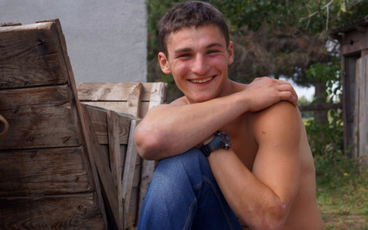 Młody mężczyzna uśmiechający się, siedzący na drewnianej skrzyni.