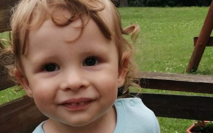 Małe dziecko z kręconymi włosami, uśmiechające się na placu zabaw.