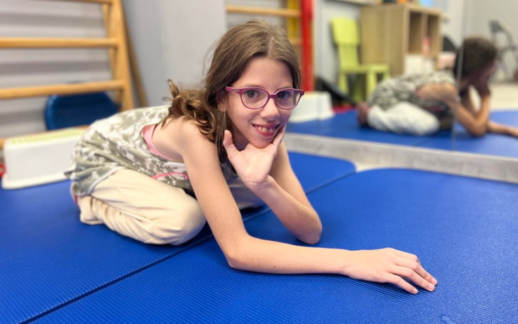 Dziewczynka w okularach, leżąca na macie do ćwiczeń.