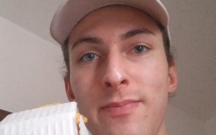 Młody mężczyzna z nakryciem głowy trzyma ciastko, usta zamknięte, półprofil w zdjęciu selfie.