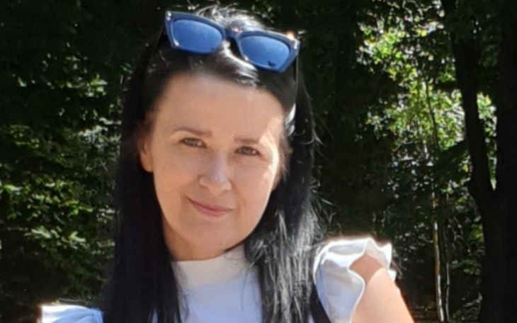Kobieta na zewnątrz, okularami na głowie, w kadrze zielone drzewo w tle