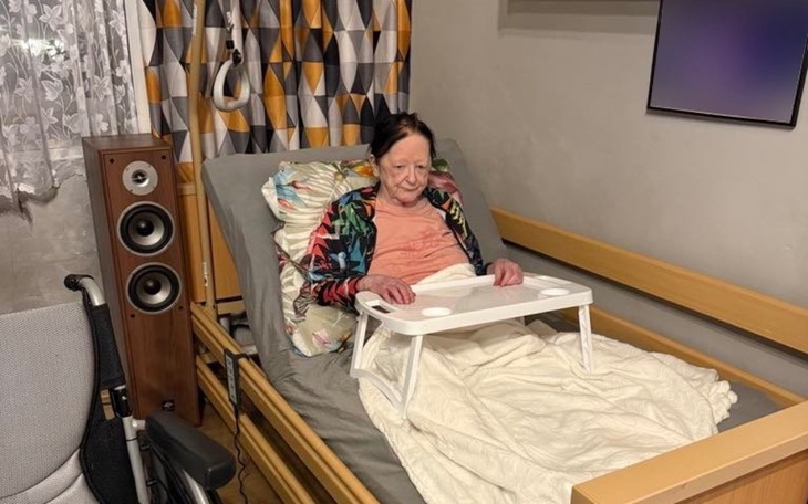 Starsza kobieta siedząca w łóżku z podkładką na stole.