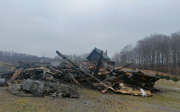 Zniszczony dom po pożarze, z ruinami w tle.