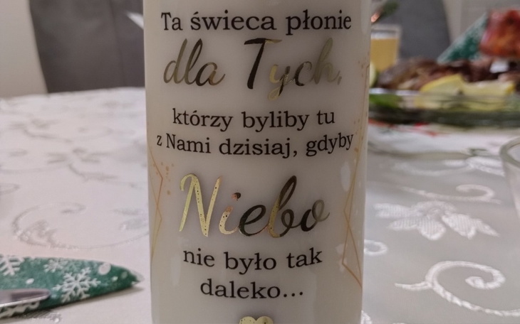 Świeca z napisem, paląca się dla zmarłych, na eleganckim stole.