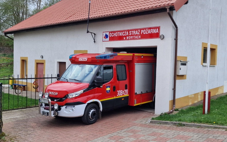 Czerwony wóz strażacki przed remizą, gotowy do akcji.